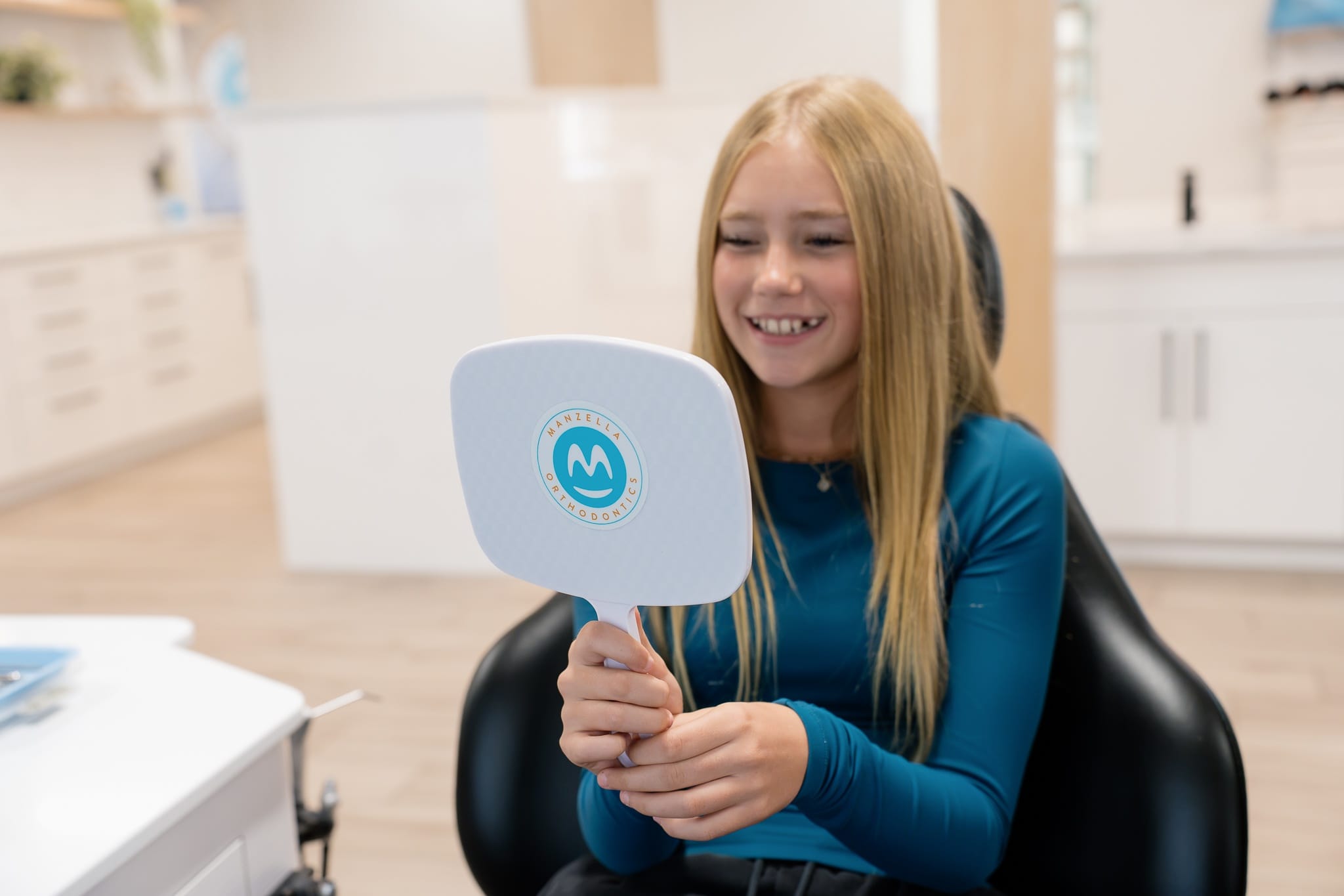 Teen patient smiling with a Manzella Orthodontics hand mirror in the treatment chair